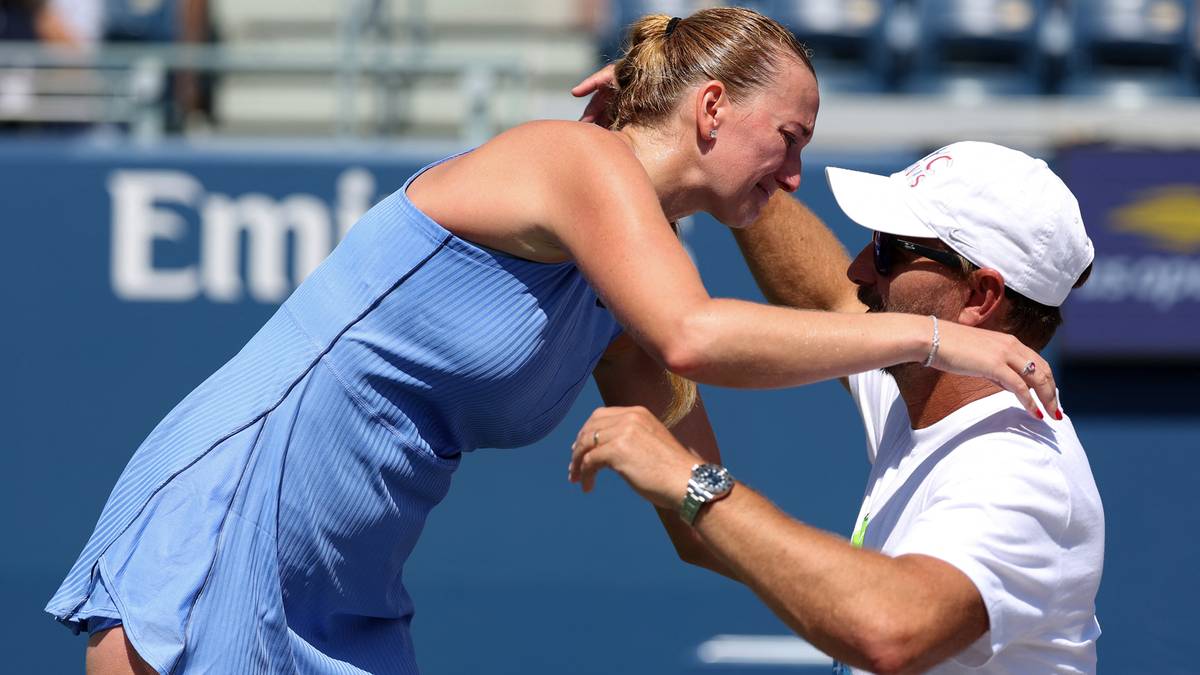 Kobieta w niebieskiej sukience tenisowej jest przytulana przez mężczyznę w białej czapce i białej koszulce. Oboje mają wzruszone twarze.