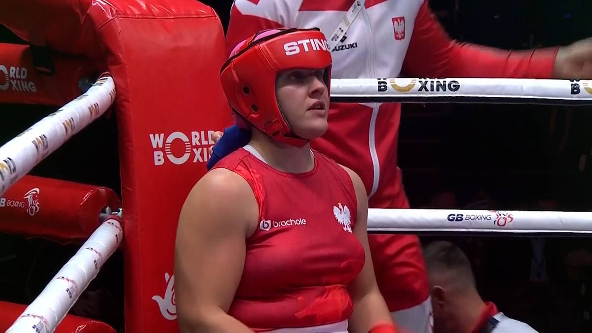 Bokserka w czerwonym stroju i kasku ochronnym patrzy w górę, gotowa do walki na ringu mistrzostw świata.