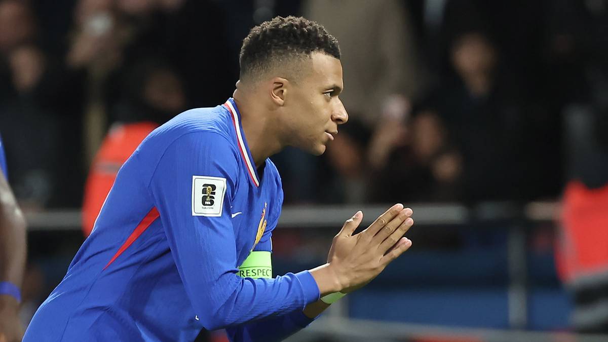 Piłkarz Kylian Mbappe w niebieskiej koszulce, z dłońmi złożonymi przed sobą, podczas meczu piłkarskiego.