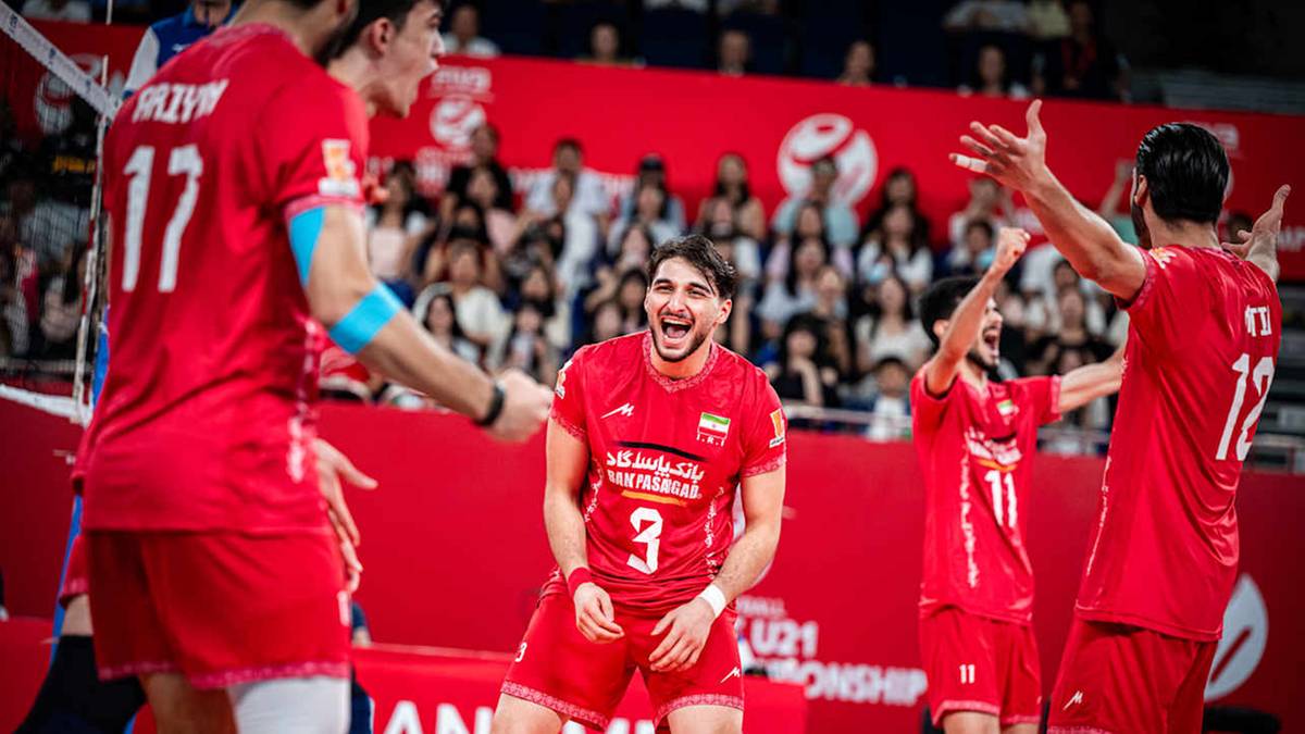 Siatkarze w czerwonych strojach świętują zwycięstwo, jeden z nich, z numerem 3 na koszulce, z szerokim uśmiechem na twarzy unosi ręce. W tle widzowie na trybunach.