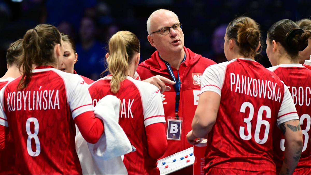 Trener piłkarki ręcznej reprezentacji Polski w czerwonej koszulce z napisem "POLSKA" rozmawia z zawodniczkami w biało-czerwonych strojach sportowych.