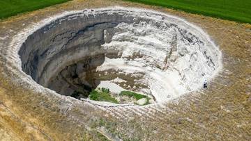 Ogromne zapadlisko o skalistych ścianach, otoczone suchą glebą i polem uprawnym.