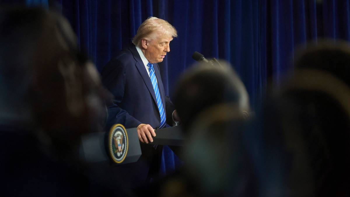 Donald Trump stoi przy m&oacute;wnicy podczas przem&oacute;wienia, ubrany w garnitur i niebieski krawat.