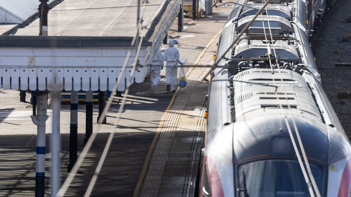 Dwie osoby w białych kombinezonach na peronie kolejowym obok pociągu