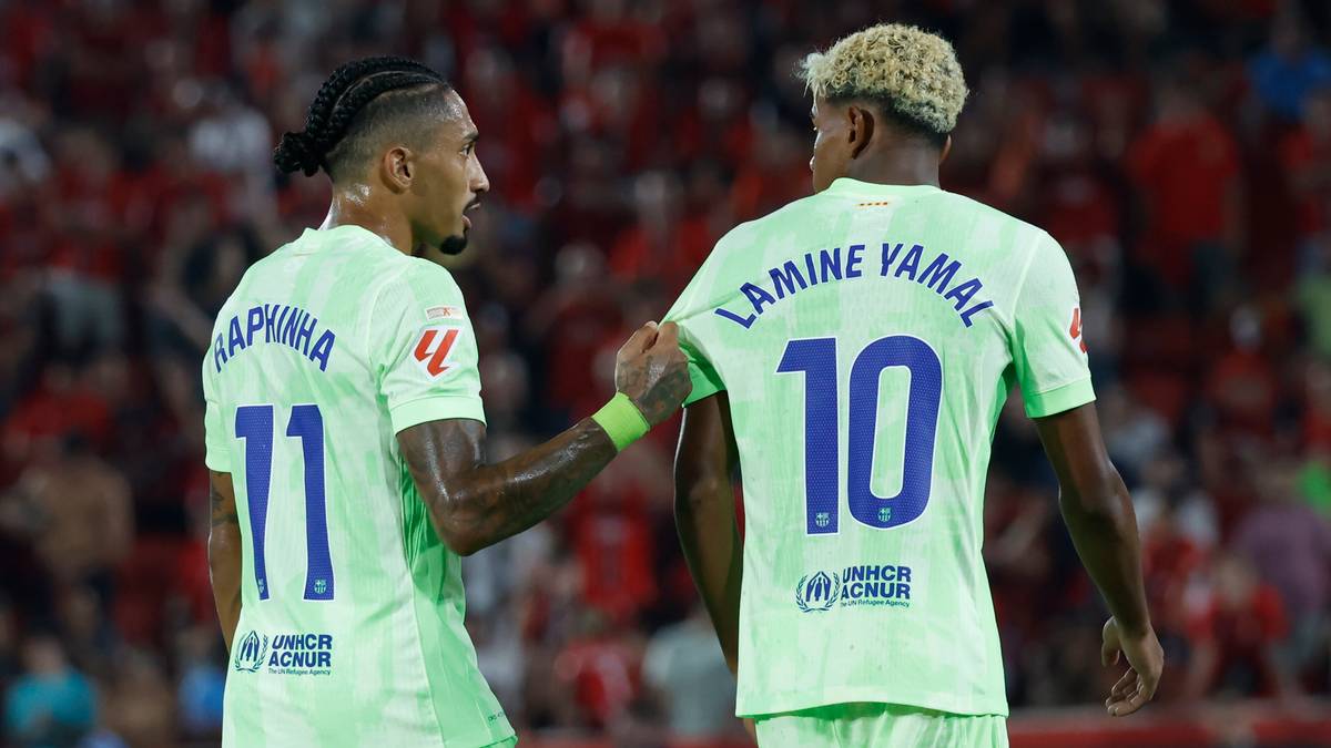 Dwóch piłkarzy FC Barcelony w jasnych zielonych koszulkach. Jeden, z numerem 11 i nazwiskiem "RAPHINHA" na plecach, klepie drugiego po ramieniu. Drugi piłkarz, z numerem 10 i nazwiskiem "LAMINE YAMAL", odwrócony plecami do widza.