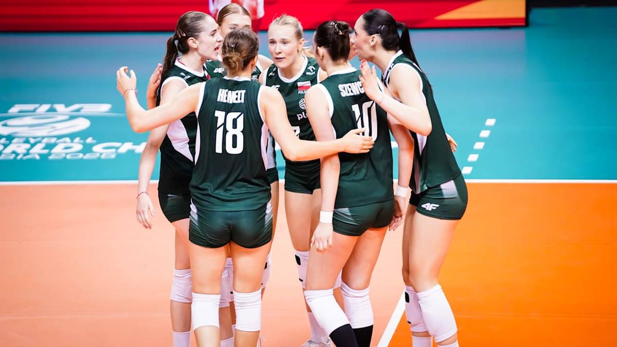 Siedem siatkarek w ciemnozielonych strojach sportowych stoi w ciasnym kręgu, przytulając się i rozmawiając między sobą podczas meczu.