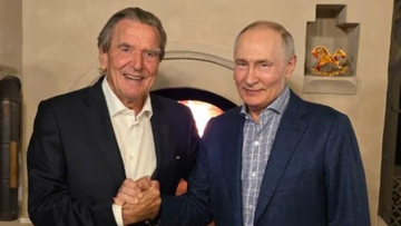 Gerhard Schr&ouml;der i Władimir Putin stojący obok siebie i ściskający sobie dłonie na tle kominka.