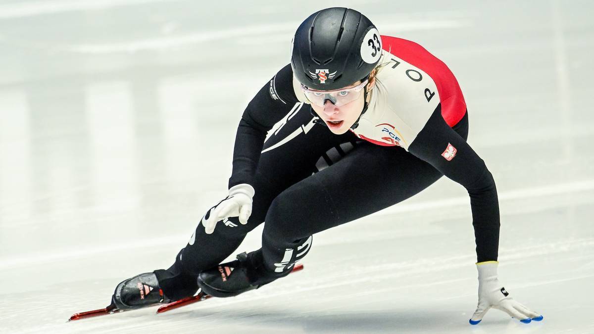 Zawodniczka short tracku w kasku i kombinezonie pochylona nad lodem podczas jazdy na łyżwach.