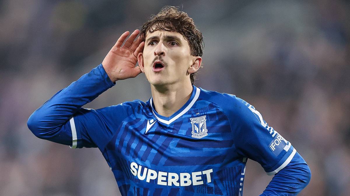 Piłkarz Lecha Poznań w niebieskiej koszulce z numerem 99 na spodenkach, gestykuluje ręką przy uchu.