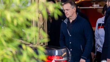 Mężczyzna w okularach i ciemnej kurtce stoi obok samochodu.