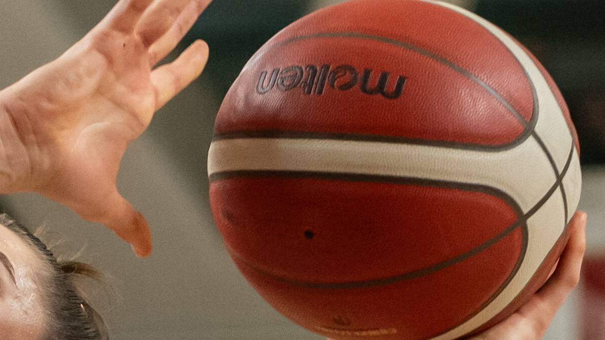 Koszykarka w białej koszulce z numerem 73 i napisem Enea rzuca do kosza, podczas gdy zawodniczka z numerem 95 w zielonej koszulce pr&oacute;buje ją zablokować.