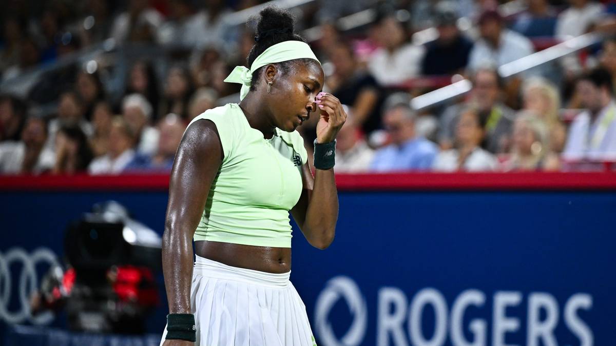 Tenisistka w jasnoniebieskiej koszulce i białej spódniczce na korcie tenisowym, z ręką przy twarzy.