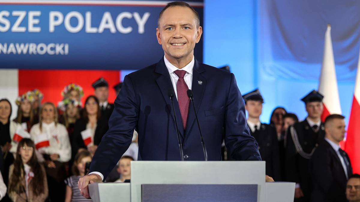 Uśmiechnięty mężczyzna w garniturze, stojący za m&oacute;wnicą z napisem "POLSKI SEJM 0%"