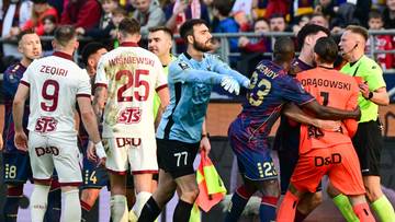 Piłkarze w trakcie konfrontacji na boisku, bramkarz w niebieskiej koszulce stara się rozdzielić zawodników.