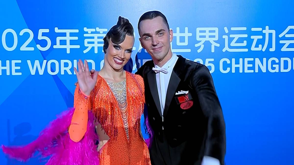 Para tancerzy w strojach tanecznych, kobieta w pomarańczowej sukni z piórami, mężczyzna w czarnym fraku, pozują z uśmiechem przed niebieskim tłem z napisem "CHENGDU 2025".