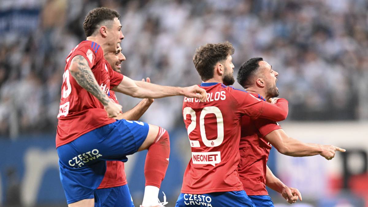 Trzech piłkarzy w czerwonych strojach świętuje na boisku.