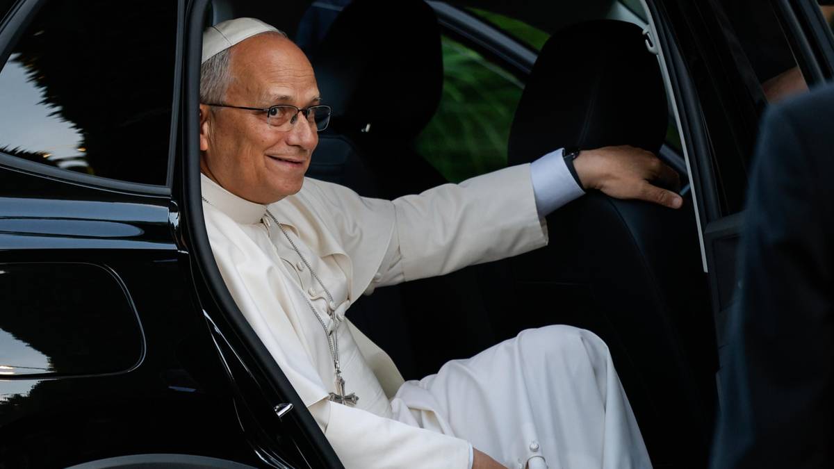 Papież Franciszek wysiada z czarnego samochodu, uśmiechając się do kogoś.