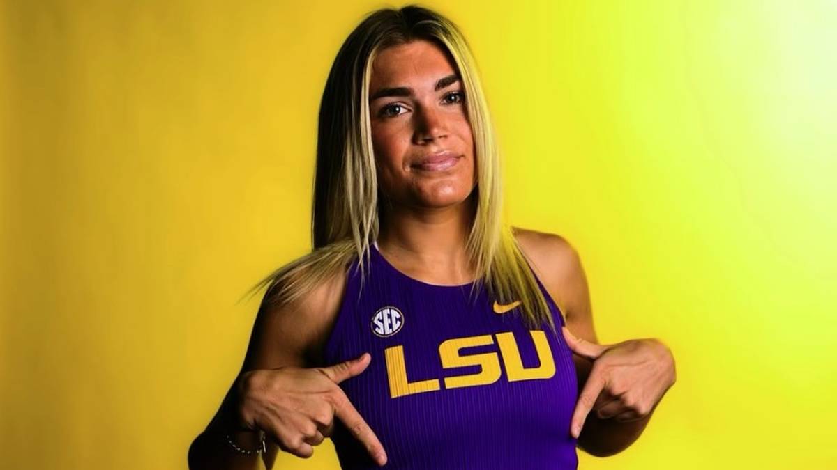 Młoda kobieta w stroju sportowym z napisem LSU wskazuje palcami na swoje ubranie.