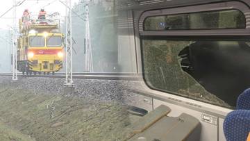 Żółty pojazd kolejowy naprawiający trakcję obok uszkodzonego wagonu z wybitym oknem.