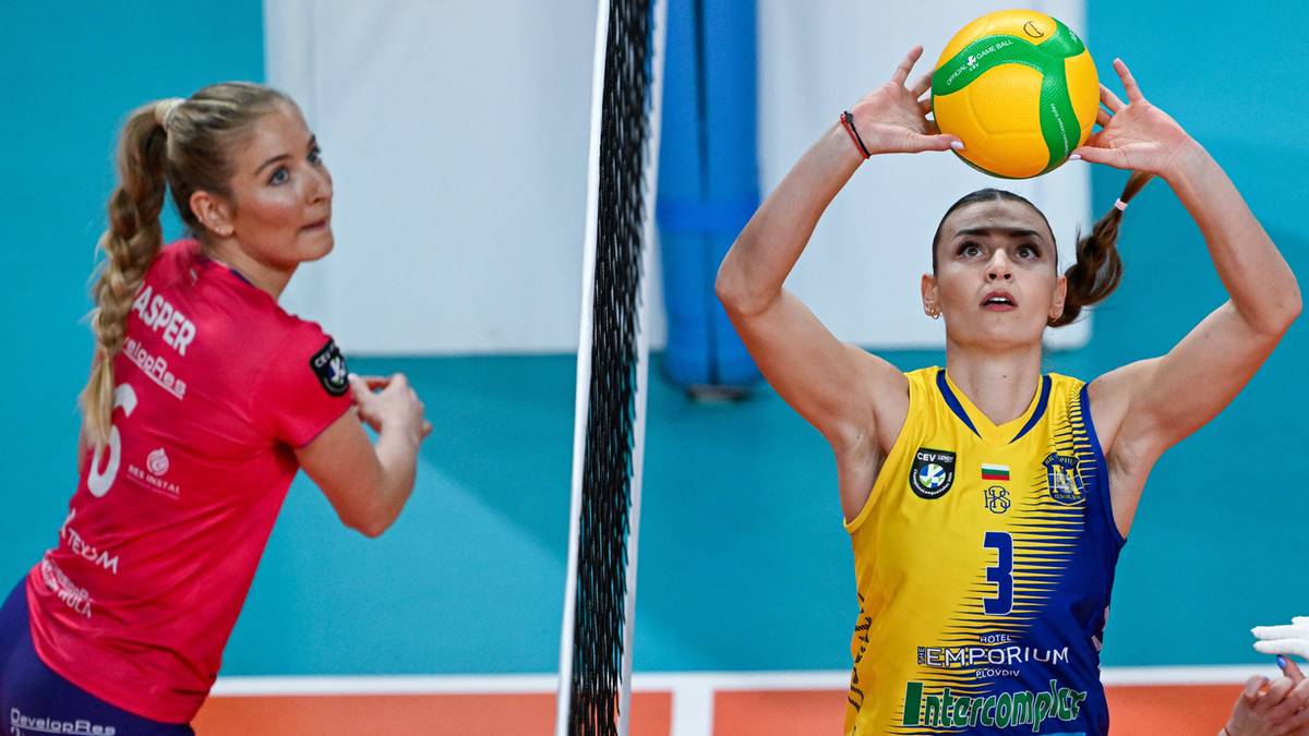 Dwie siatkarki na boisku, jedna przygotowuje się do zagrywki, druga do przyjęcia piłki.