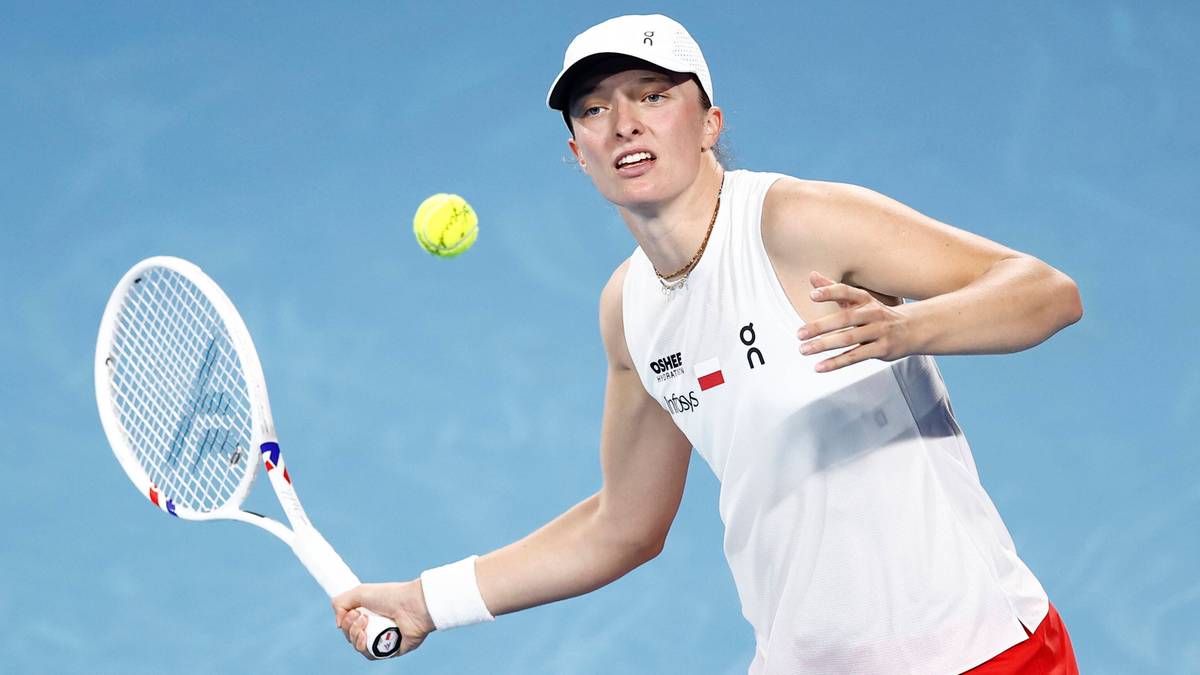 Tenisistka w białej koszulce i czerwonych spodenkach odbija piłkę rakietą.