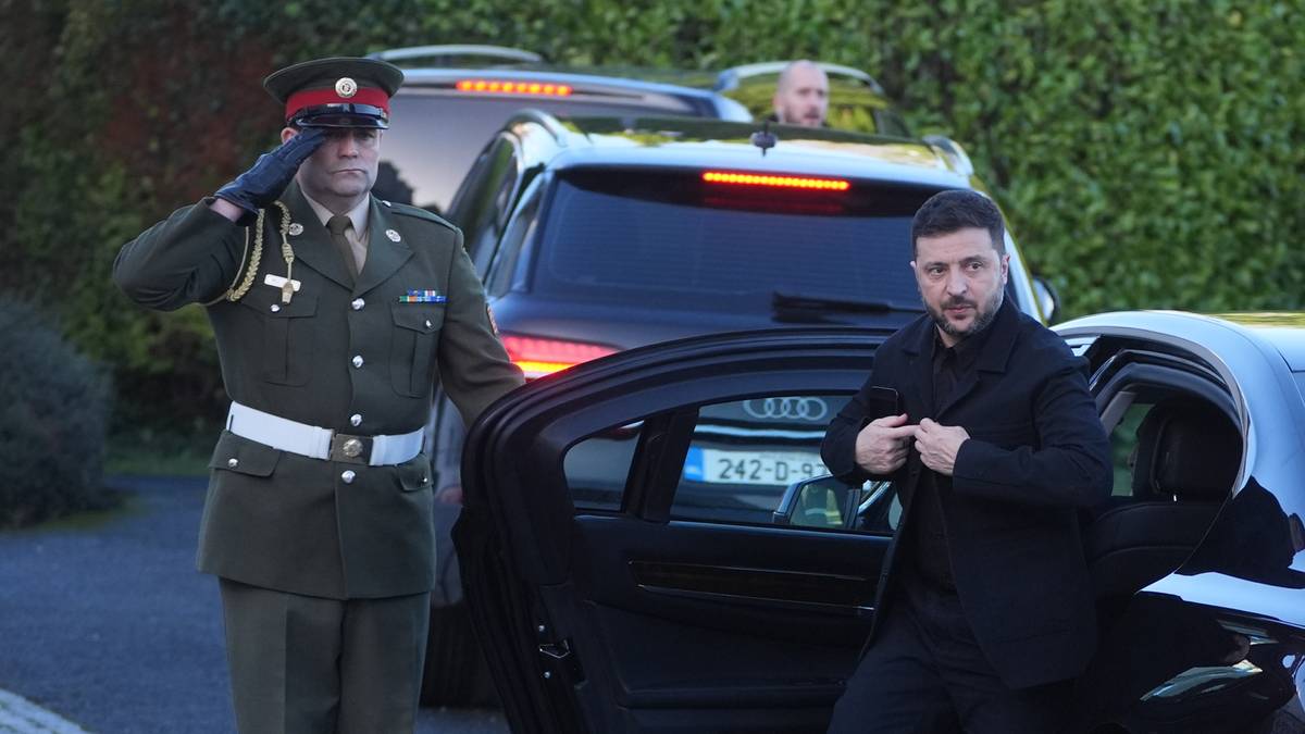 Żołnierz w mundurze salutuje obok otwartych drzwi samochodu, z którego wychodzi mężczyzna w garniturze.