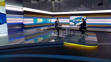 Dwaj mężczyźni siedzą przy okrągłym stole w nowoczesnym studio telewizyjnym podczas nagrania programu.
