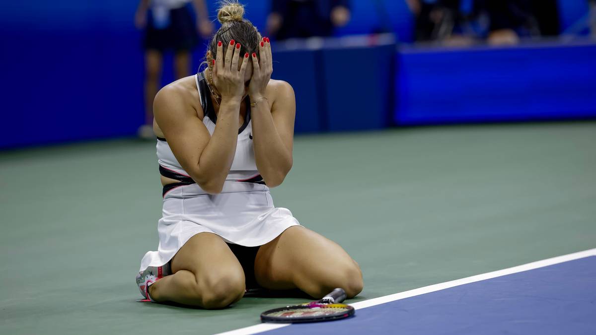 Aryna Sabalenka klęczy na korcie tenisowym, zakrywając twarz dłońmi.