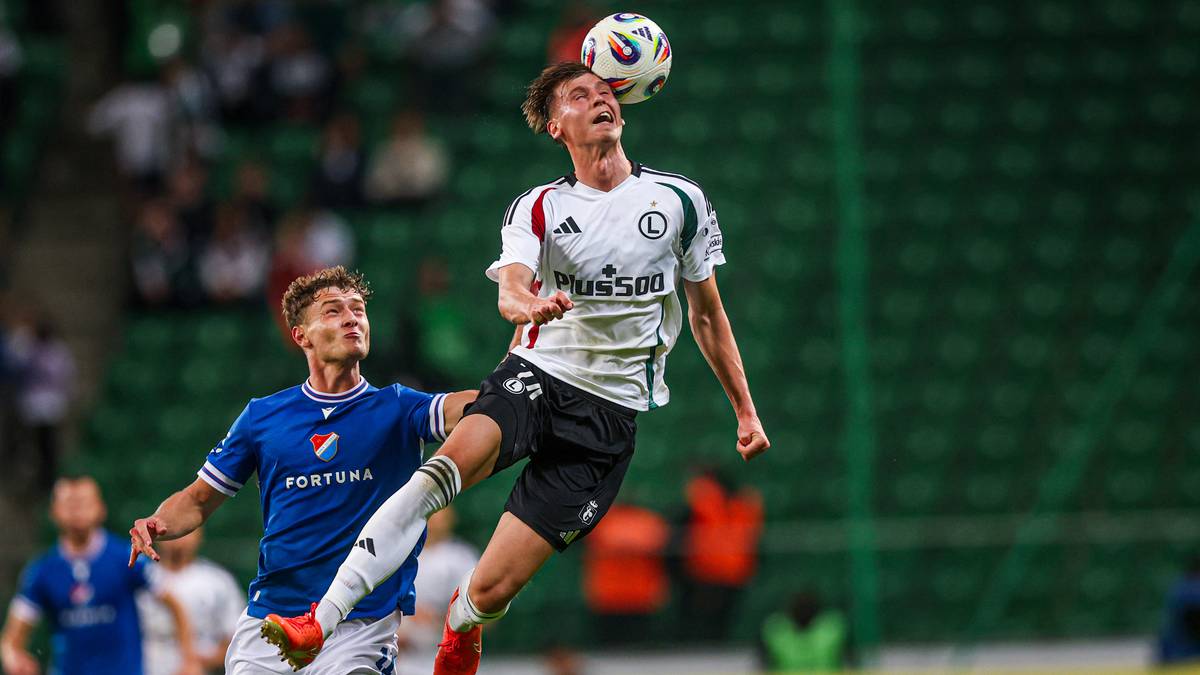 Piłkarz Legii Warszawa w białej koszulce z czarnymi spodenkami próbuje zagrać głową piłkę lecącą w powietrzu.