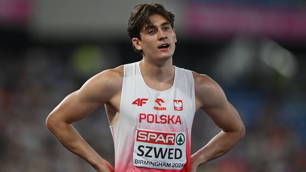 Młody mężczyzna w białej koszulce sportowej z napisem "POLSKA" i "SPAR SZWED" na tle stadionu.