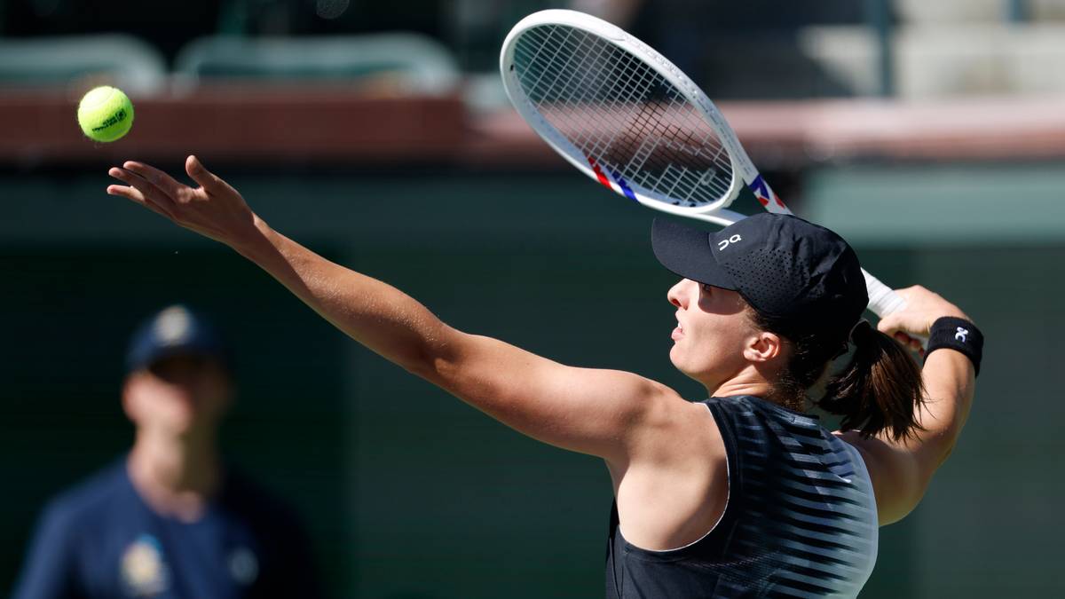 Tenisistka Iga Świątek wyrzuca piłkę do g&oacute;ry, przygotowując się do serwisu podczas meczu.