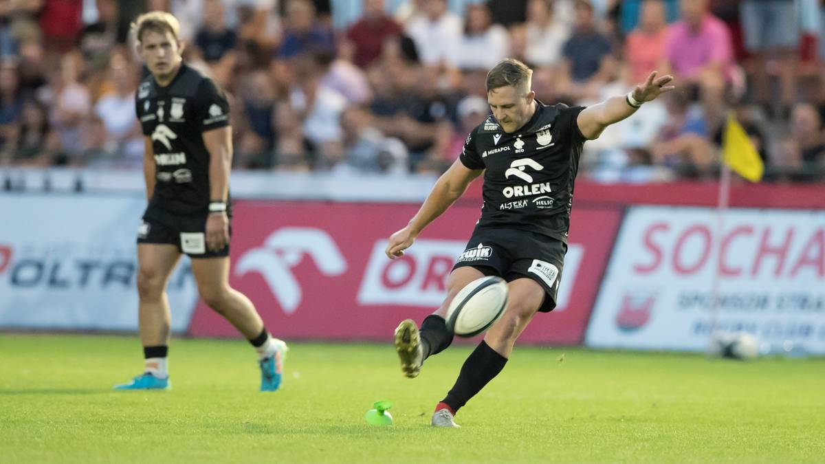 Rugbysta w czarnej koszulce z białym napisem "ORLEN" kopie piłkę.