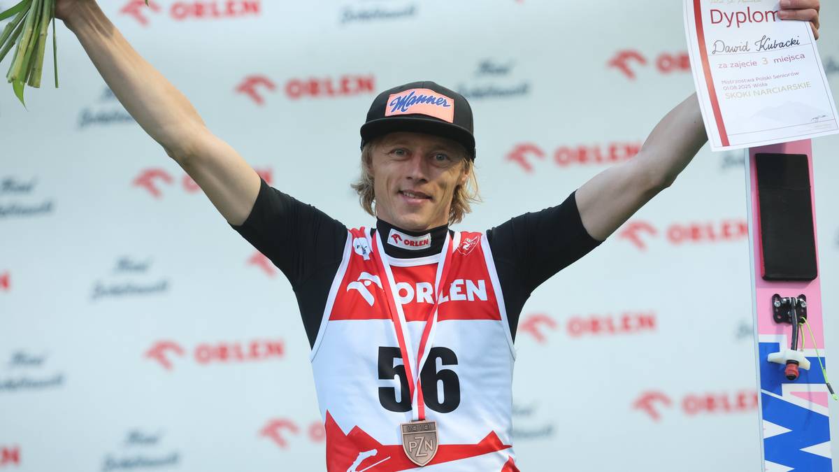Dawid Kubacki, polski skoczek narciarski, stoi na podium z podniesionymi ramionami, trzymając bukiet kwiatów w lewej ręce i dyplom w prawej. Na szyi ma medal z numerem 56, a na piersi koszulkę z logo ORLEN.