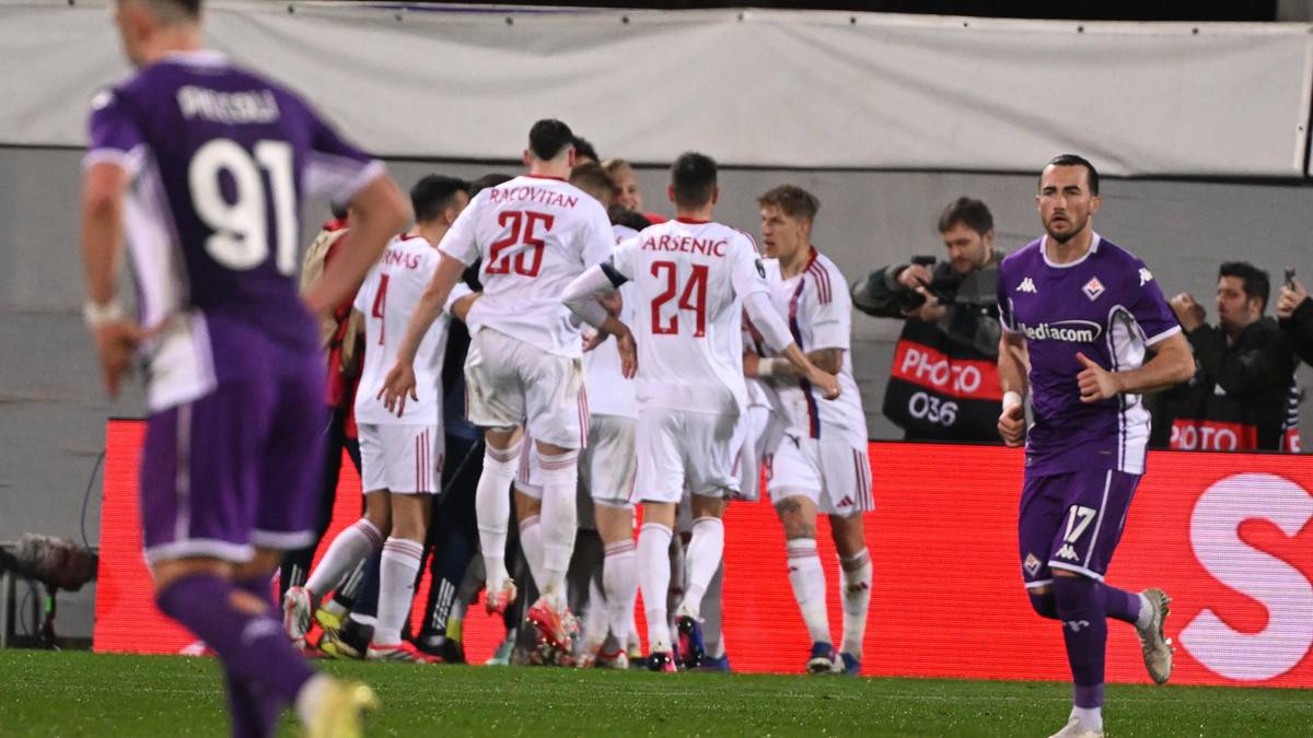 Piłkarze w białych i fioletowych strojach świętujący bramkę na boisku.