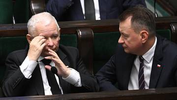 Dwóch polityków w garniturach siedzi w ławach sejmowych. Starszy mężczyzna z siwymi włosami przeciera oczy dłońmi, obok niego siedzi drugi mężczyzna.