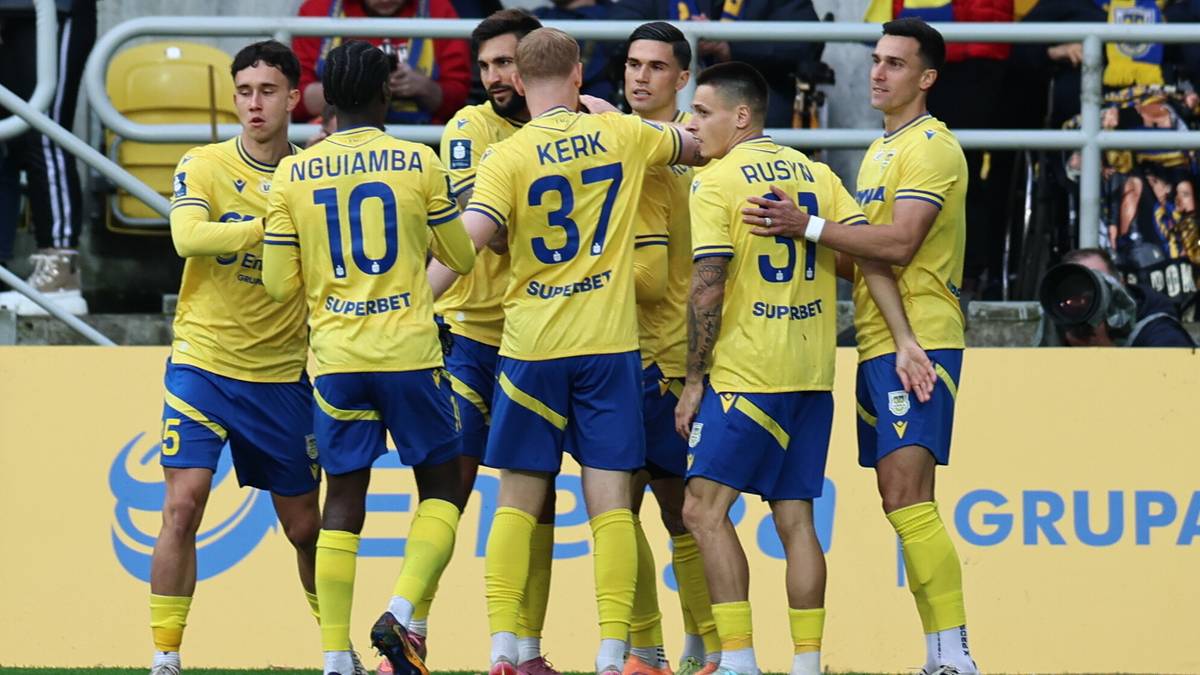 Siedmiu piłkarzy w ż&oacute;łtych koszulkach i niebieskich spodenkach stoi w p&oacute;łokręgu, rozmawiając ze sobą.