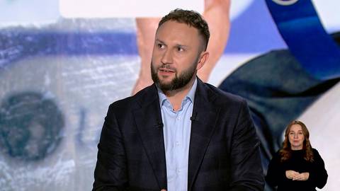 Portret Konrada Niedźwiedzkiego podczas wywiadu, z tłumaczem języka migowego w tle.