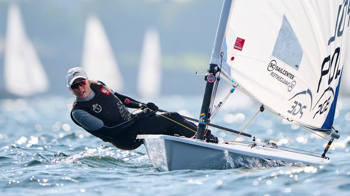 Kobieta w stroju sportowym na małym żagl&oacute;wce pochyla się, aby utrzymać r&oacute;wnowagę podczas regat.