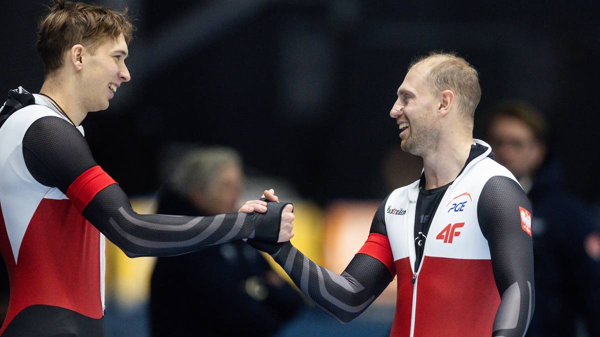 Dwóch łyżwiarzy szybkich w strojach narodowych Polski, w geście gratulacji po zawodach, ściska sobie dłonie.