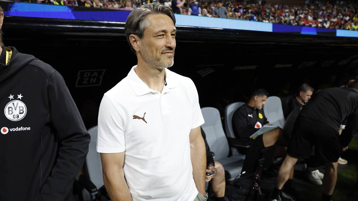 Trener piłkarski Edin Terzić w białej koszulce polo z logo Pumy stoi na boisku.