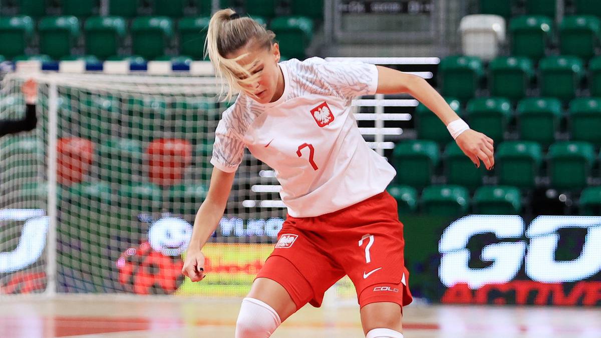 Dwie zawodniczki w białych strojach sportowych grają w piłkę nożną halową na parkiecie.