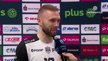 Paweł Zatorski, siatkarz, w białej koszulce sportowej z czarnymi elementami, udziela wywiadu trzymając mikrofon.