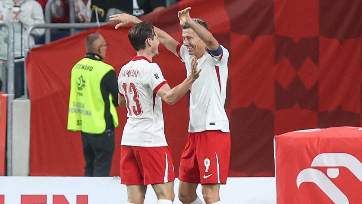 Dwóch piłkarzy w białych koszulkach z orłem na piersi i czerwonych spodenkach radośnie celebruje zdobycie bramki.