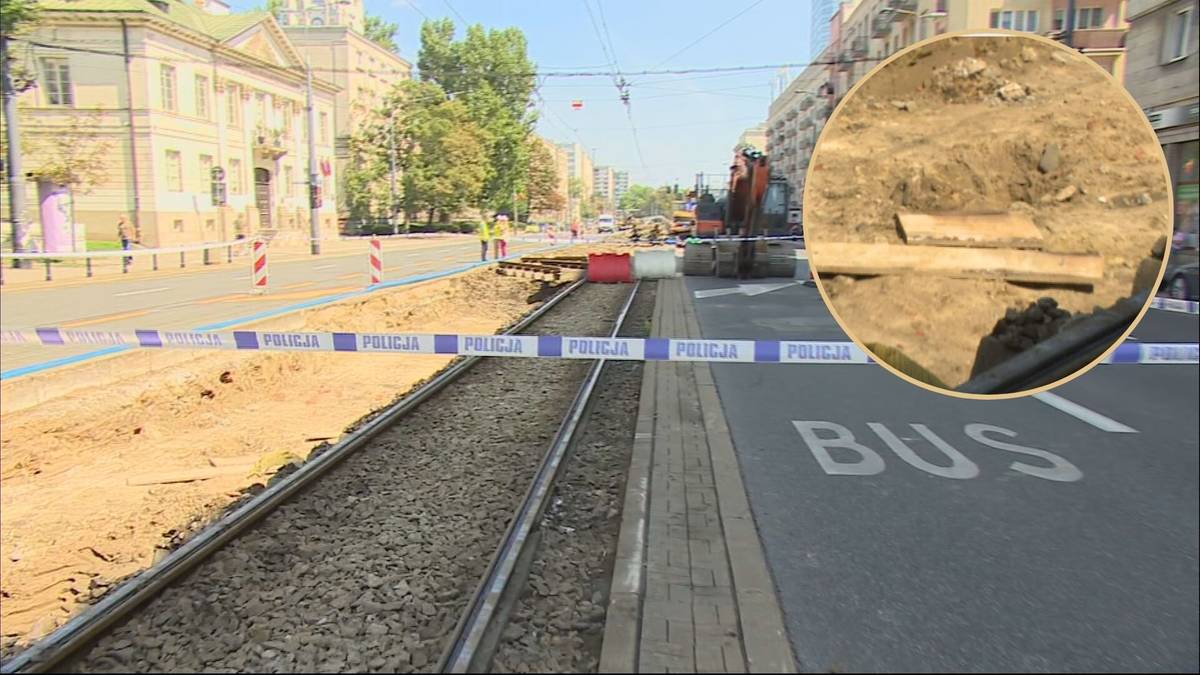Widok na torowisko tramwajowe w trakcie remontu. Po lewej stronie widoczne wykopy i taśma ostrzegawcza. W oddali budynki i pracujący człowiek. W prawym g&oacute;rnym rogu zbliżenie na odkryte rury.