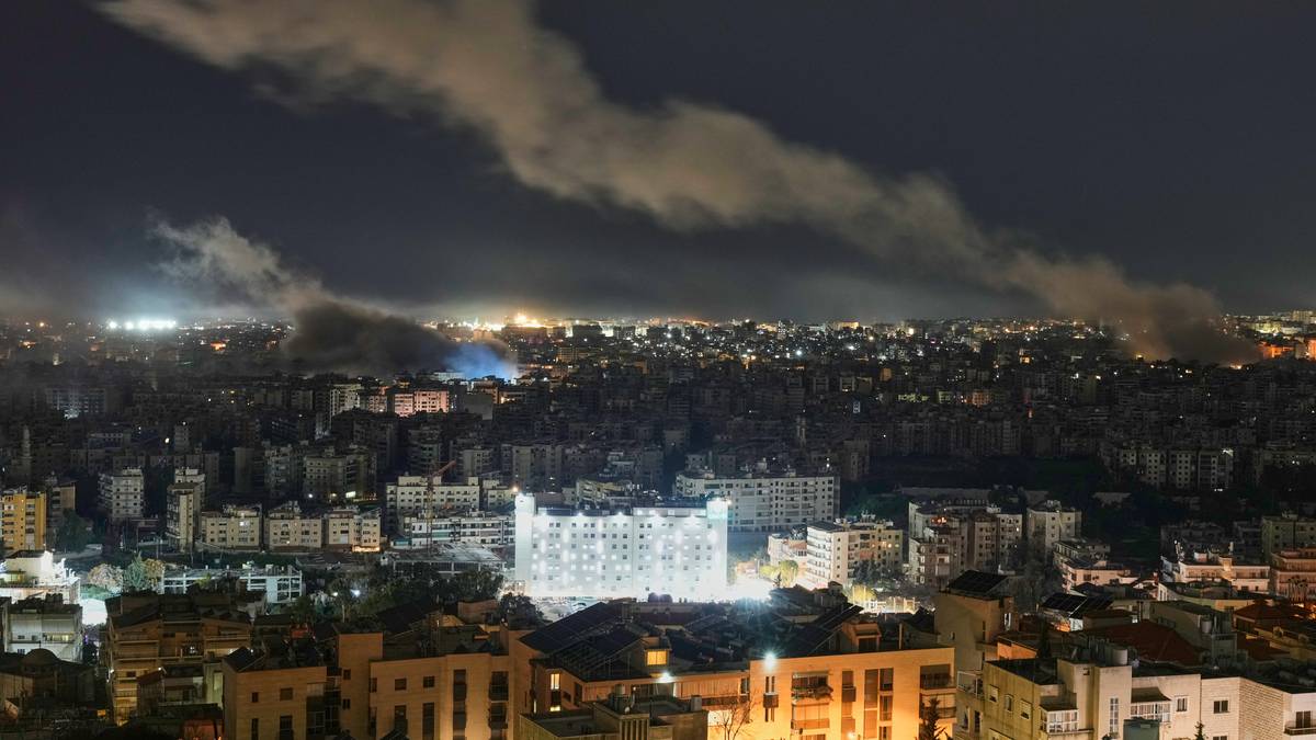 Nocny widok miasta z dymem unoszącym się nad zabudowaniami, wskazującym na pożar lub eksplozję.