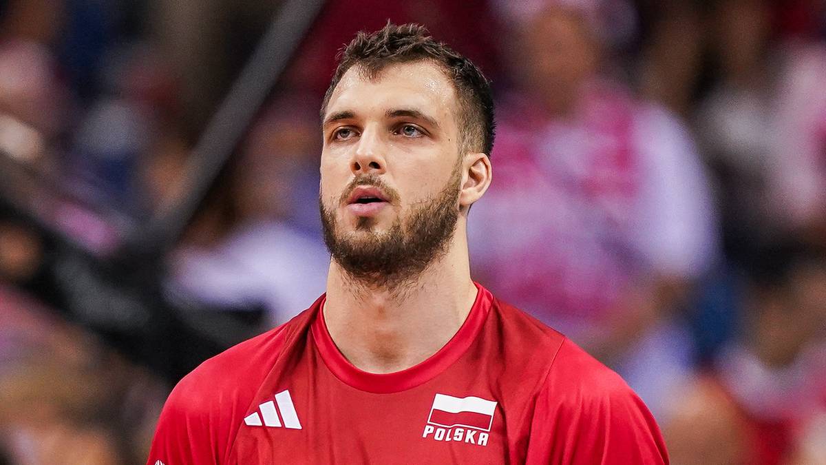 Trzech siatkarzy w czerwonych strojach z białymi numerami na plecach.