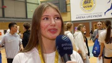 Portret młodej kobiety z długimi blond włosami, z medalem na szyi, trzymającej mikrofon w ręce.