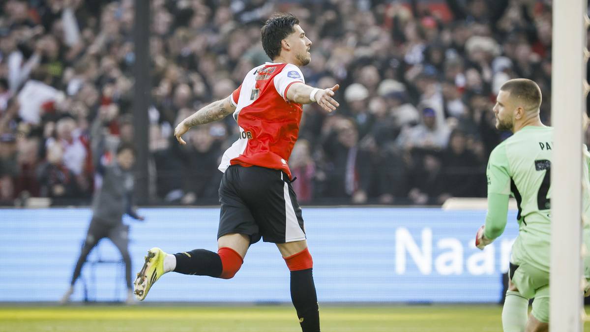 Piłkarz Feyenoordu w czerwono-białej koszulce biegnie po boisku z uniesioną ręką, celebrując bramkę. Obok niego klęczy przeciwnik.