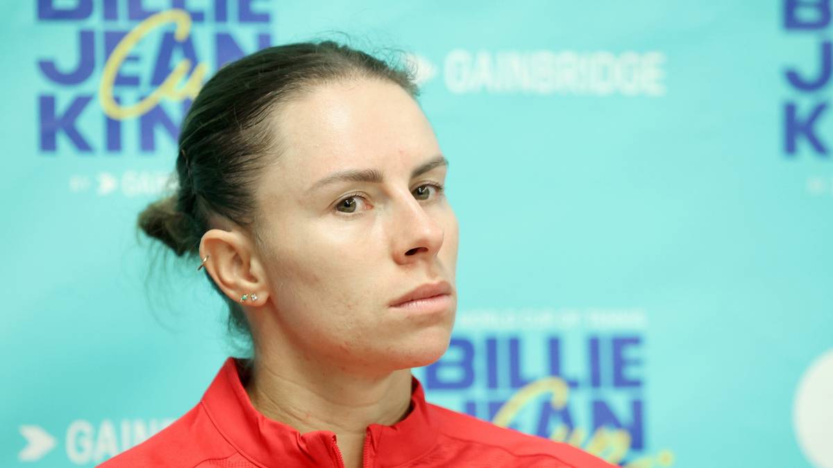 Portret tenisistki Magdy Linette w czerwonej bluzie, z logo Billie Jean King Cup w tle.