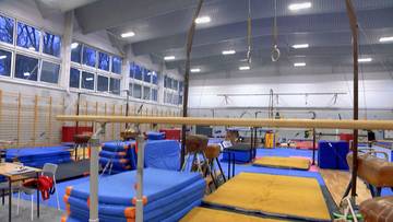 Sala gimnastyczna z drążkiem, k&oacute;łkami gimnastycznymi, skrzynią i materacami.